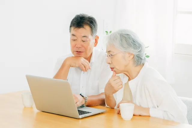 年配の夫婦がノートパソコンの画面を見ながら考えている様子