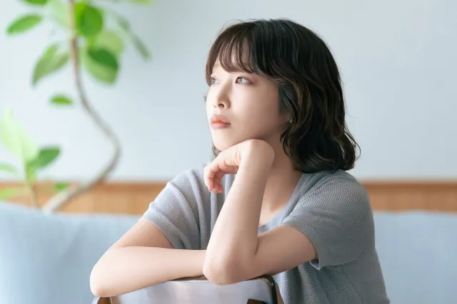 椅子の背もたれ側に座って背もたれに手を置き頬杖をする悩んでいる女性