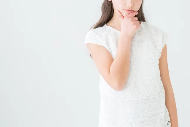 右手の親指と人差し指で顎を掴んで考えている白い服の女性