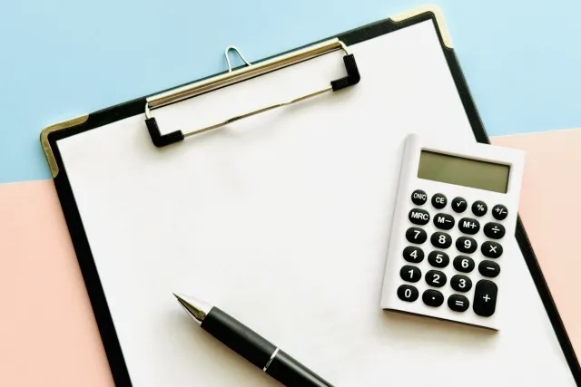 バインダーに挟まれている白紙の紙の上に電卓とボールペンが置かれている