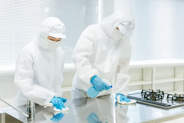 防護服を着てキッチン台を清掃する男女