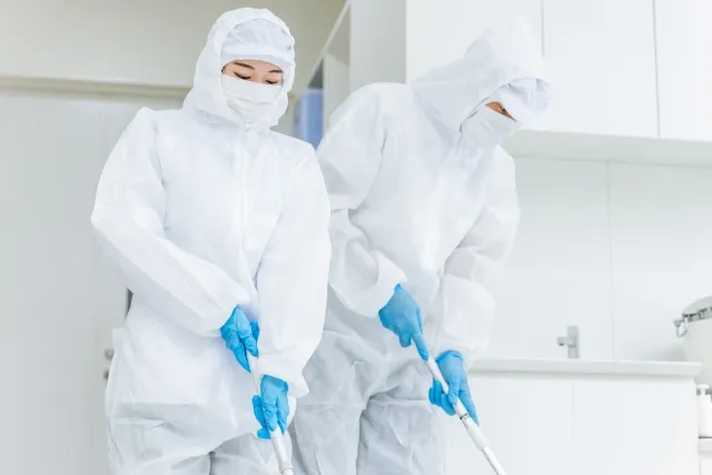防護服を着てモップで床を清掃する男女