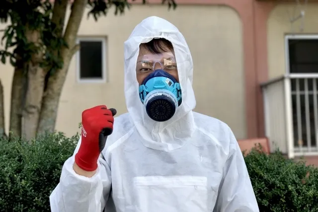 防護服着て防毒マスクを付けている男性が右手でガッツポーズしている