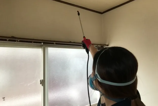 防毒マスクをしながら天井付近の壁に消毒液をかけている様子