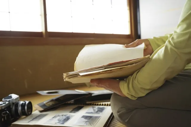遺品整理で写真集を抱えて見ている年配女性の手