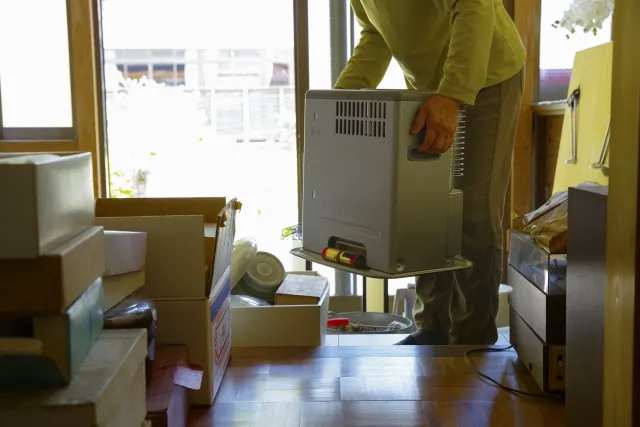 遺品整理で石油ストーブを持ち上げている年配女性
