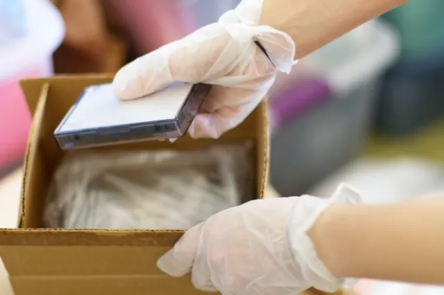 遺品整理でカセットテープを小さいダンボールに入れているビニール手袋をしている手