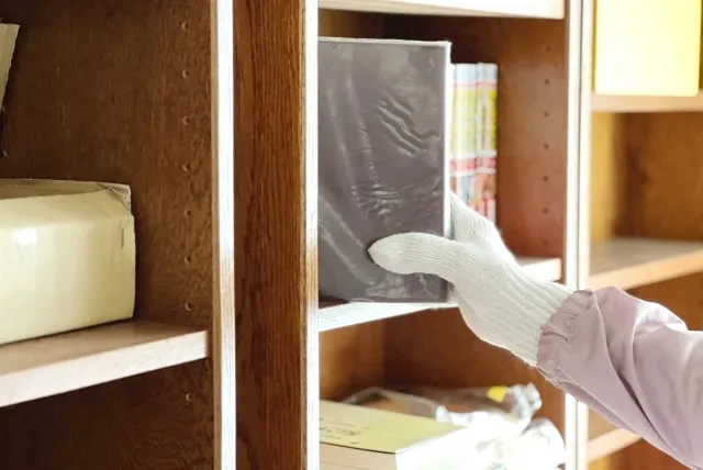 遺品整理で軍手をして本棚から本を抜き取ろうとしている手