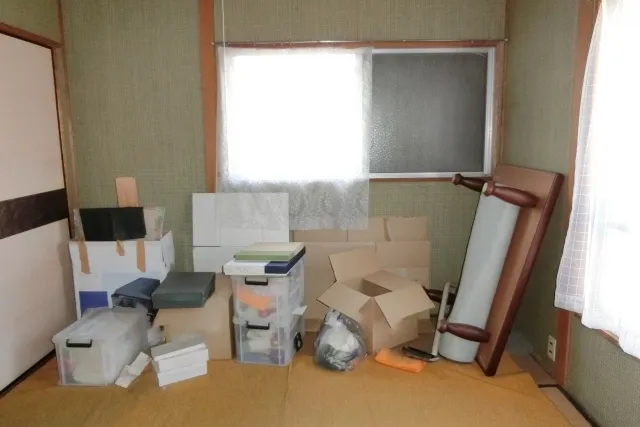 透明プラスチックケースやダンボール、木製の座卓などの不用品が置かれている部屋