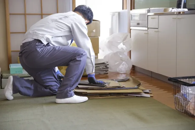 作業着を着た男性がたたんだダンボールを重ねて片付けようとしている