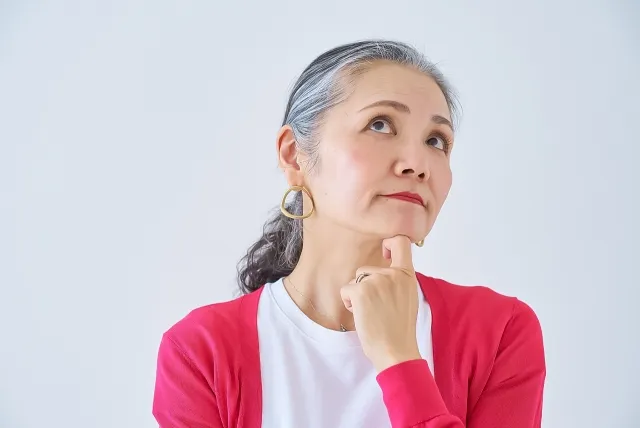 顎に指を当てて考え事をしている赤い上着を着た年配の女性