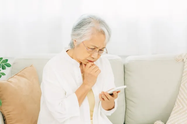 スマホを見ながら考えている白いシャツをきた年配の女性