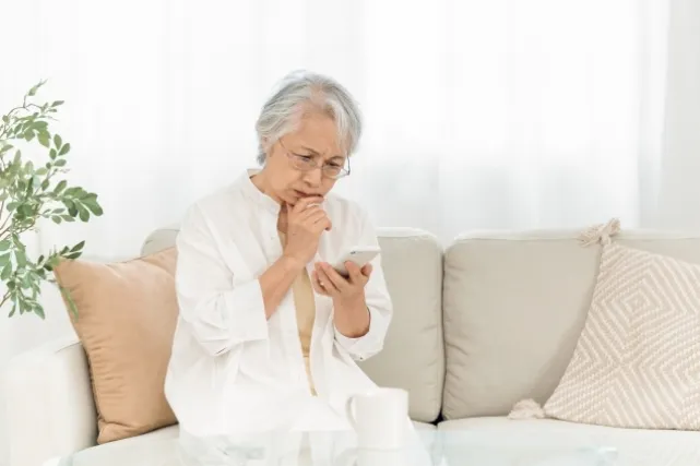 スマホを見ながら考えている様子の白いシャツを着ている年配の女性