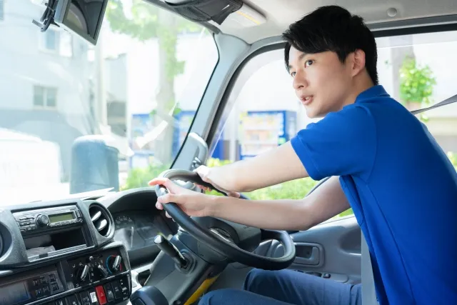 トラックを運転している引っ越し業者の青色の半そで作業着を着た男性