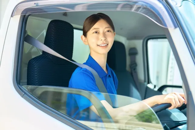 トラックを運転している引っ越し業者の青色の半そで作業着を着た女性