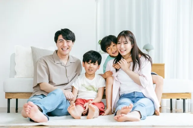自宅のソファの前で微笑んでいる若い夫婦とその子供の兄弟2人