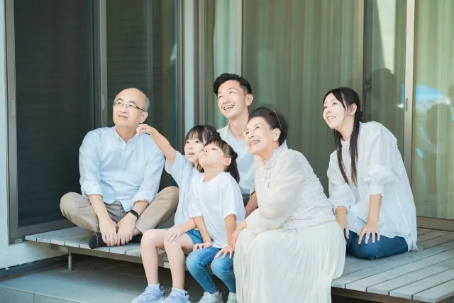 老夫婦とその子供夫婦、さらにその子供の小さい姉妹2人の3世代がベランダで微笑んで楽しんでいる様子