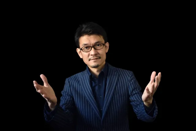 ストライプのスーツを着て眼鏡をかけて、両手を大きく広げている悪徳業者のイメージの男性