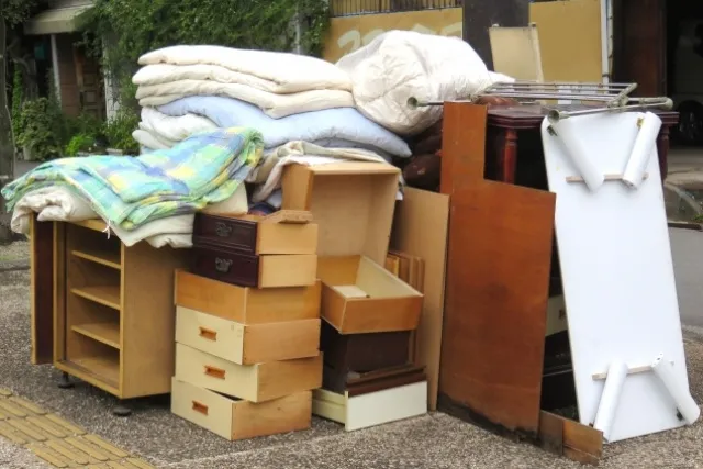 不要品の木製チェストや引き出し、座卓、布団などが積まれている