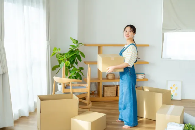 部屋でダンボールに物を入れて引っ越しの準備をしている女性