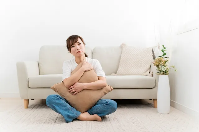 ソファの前に座ってクッションを抱いて悩んでいる女性