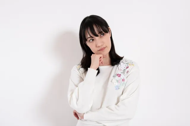 右手を顎に当てて左手で右手の肘を支えながら悩んでいる白い服を着た女性