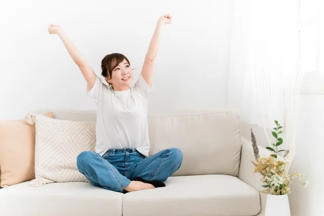 ソファーに座って拳を握りながら両手をあげてガッツポーズをする女性