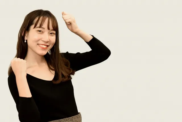 両手の拳を握ってガッツポーズを笑顔でしている黒い服を着た女性