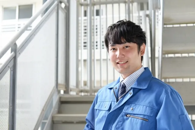 青い作業着を着た男性が階段の踊り場で微笑んでいる