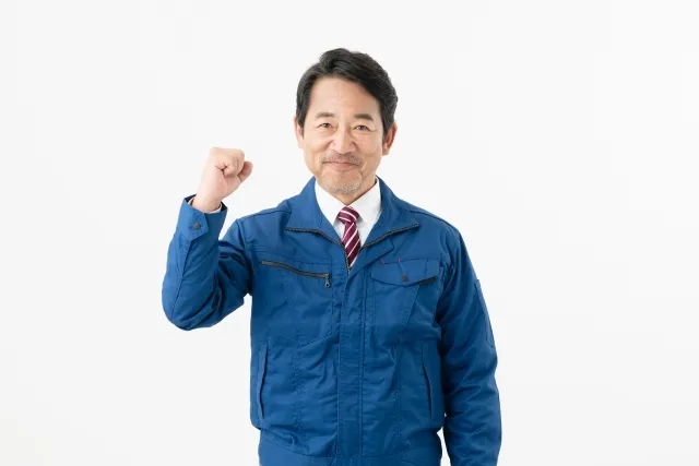 青い作業着を着た年配の男性が右手でガッツポーズをしている