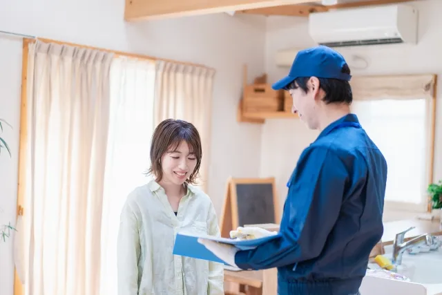 手に持ったファイルを女性に見せている青い帽子を被って青い作業着を着た男性