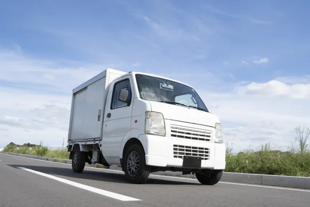 青空と荷物を運ぶ荷台の付いた軽トラック