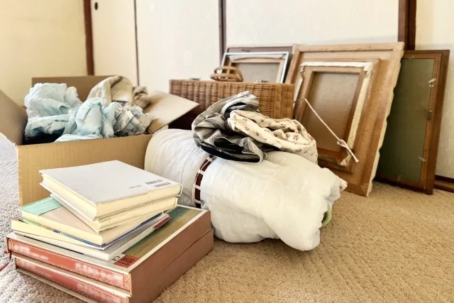 部屋の絨毯の床に置かれた額縁や本などの荷物