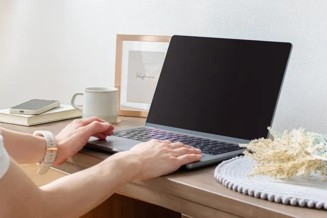 テーブルに置いたノートパソコンを操作している両手のアップ