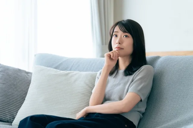 ソファの背もたれにもたれながら右手を顎に当てて考えている女性