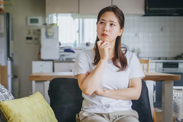 自宅の椅子に座って右手を顎に当てて考えている女性