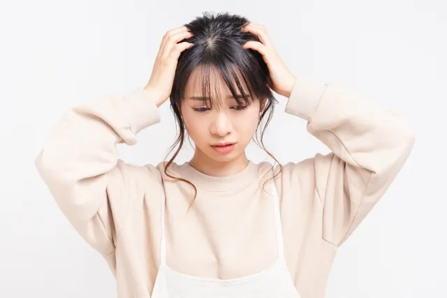 両手を頭に当てて考えている女性